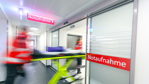 Notaufnahme Blick zum Eingang der Notaufnahme. Mit dynamischer Unschärfe ist der Rettungsdienst zu erkennen, wie dieser eine Trage in die Notaufnahme rollt.