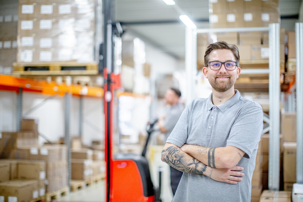 Ein Mitarbeiter der Logistik seht im Lager und blickt lächelnd zur Kamera