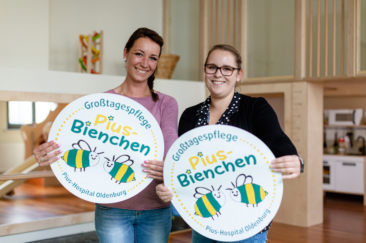 Pius Bienchen Zwei Mitarbeiterinnen der Kita "Pius-Bienchen" des Pius-Hospital Oldenburg halten zwei runde Schilder mit dem Logo in die Kamera
