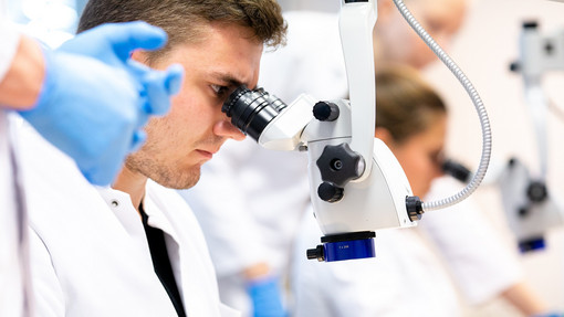 Studium Ein Medizinstudent der Augenheilkunde blickt durch ein Mikroskop