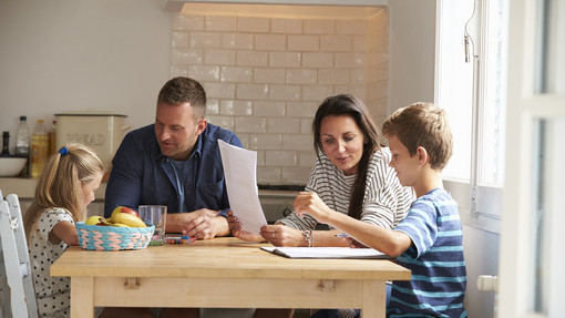 Familie und Beruf Eine Familie mit Tochter, Vater, Mutter und Sohn sitzen gemeinsam Zuhause am Tisch
