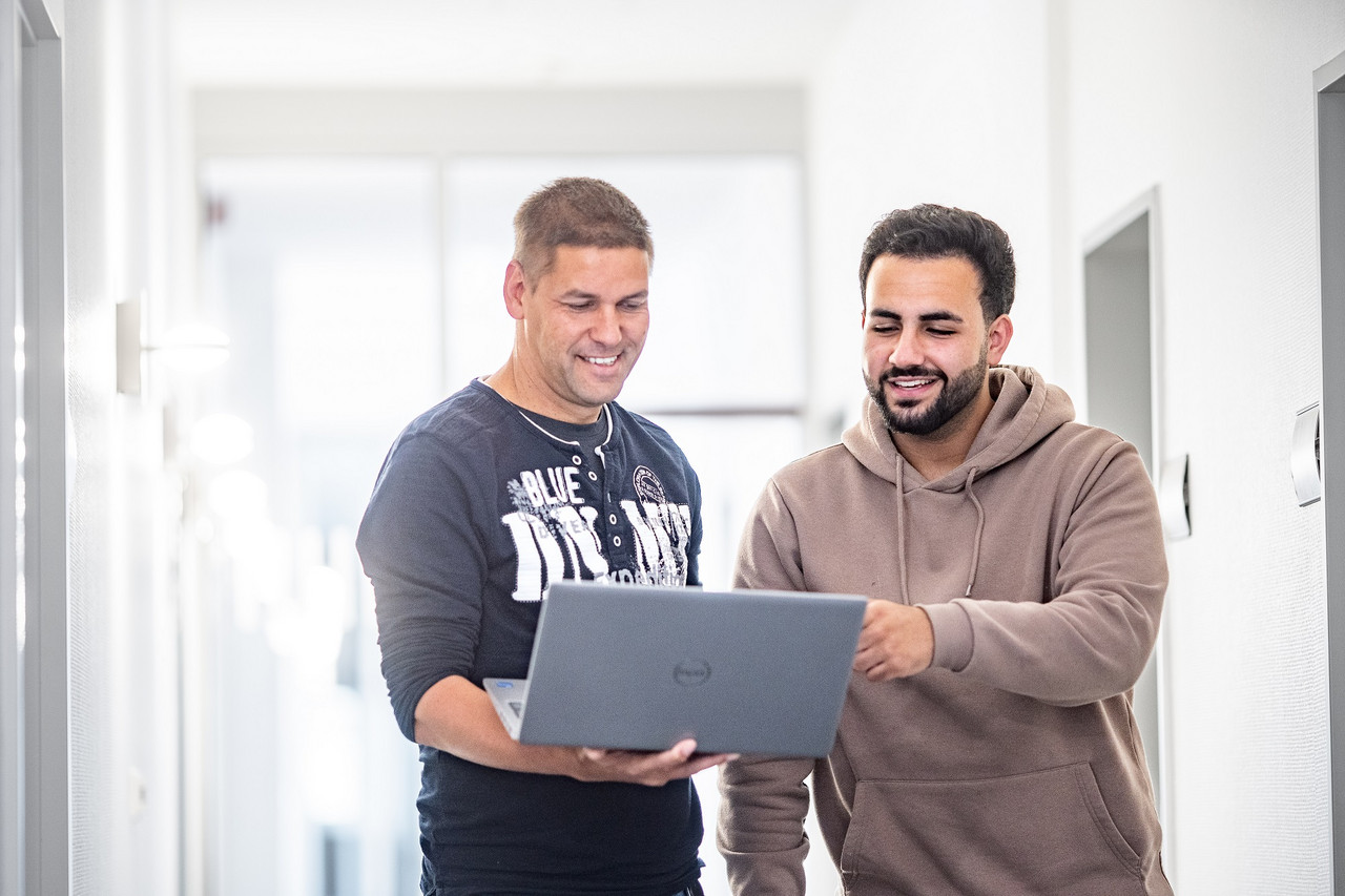 Zwei Mitarbeiter der IT blicken auf den Monitor eines Laptops