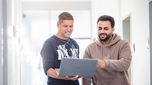 Mitarbeiter IT mit Laptop Zwei Mitarbeiter der IT blicken auf den Monitor eines Laptops
